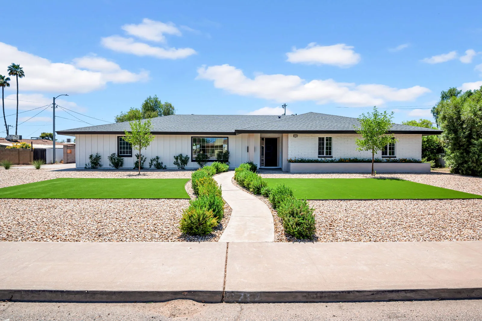 Mid-century Phoenix ranch behind a green front lawn with a curved walkway and desert plantings.