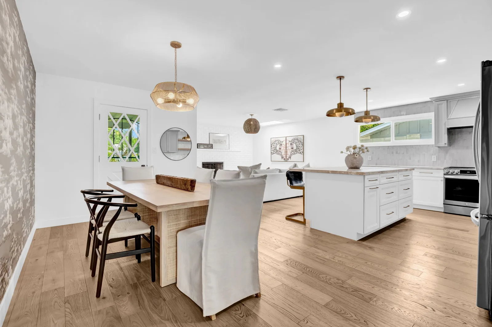 Dining table beside an open white kitchen with brass pendants.