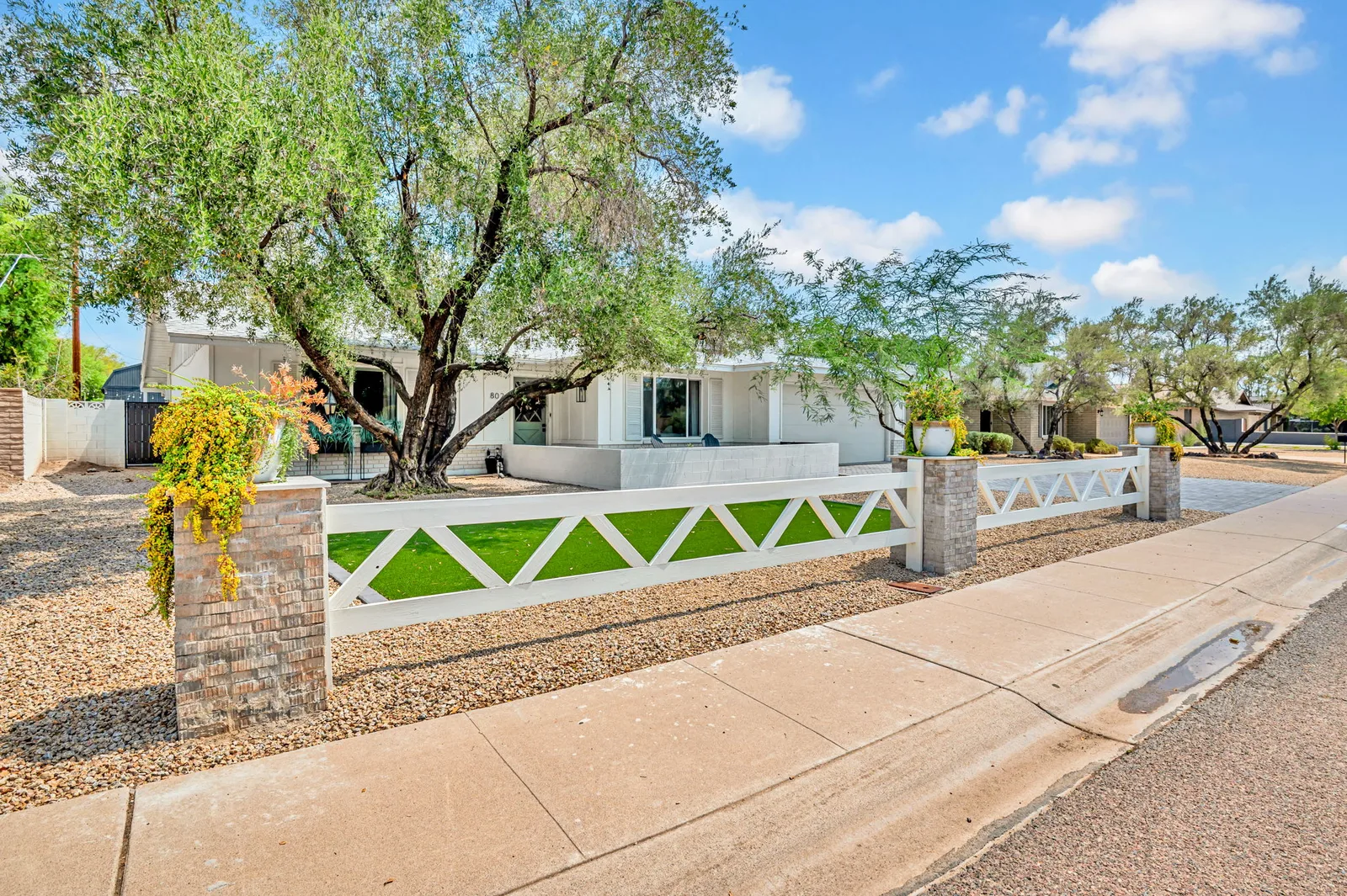 Street view of a white ranch with a decorative block wall and desert plantings.