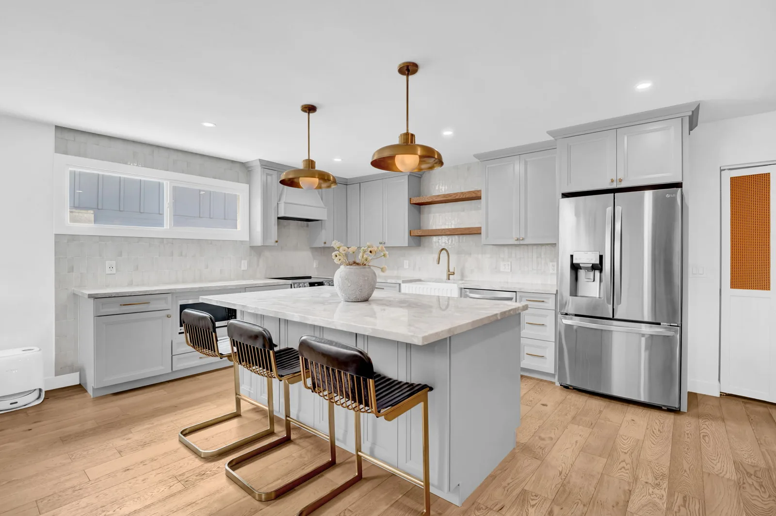 Kitchen island with brass pendants, waterfall counter and bar stools.