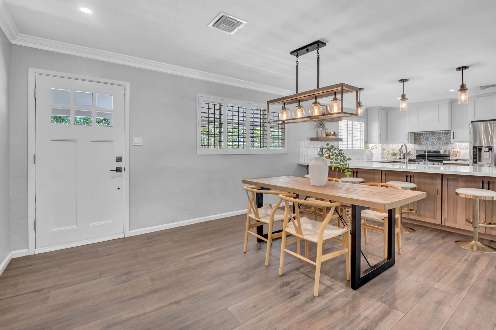 Open kitchen and dining with a linear iron chandelier and plantation shutters.