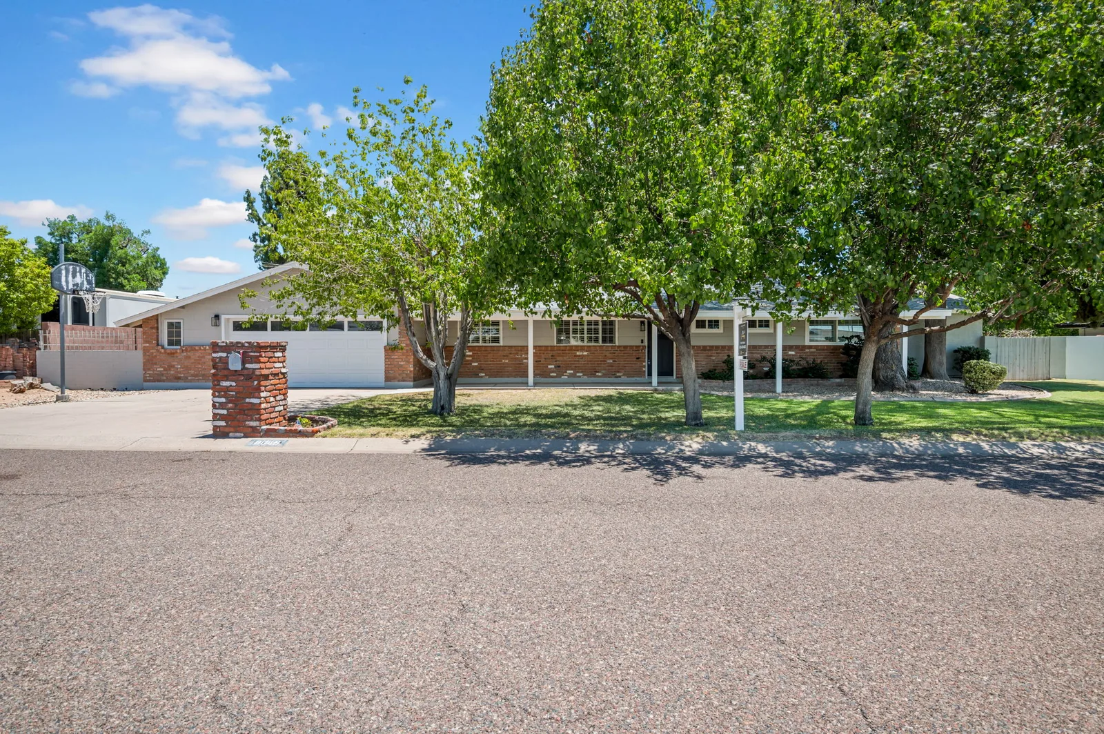 Long ranch home set back behind a deep flood-irrigated lawn and old shade trees.