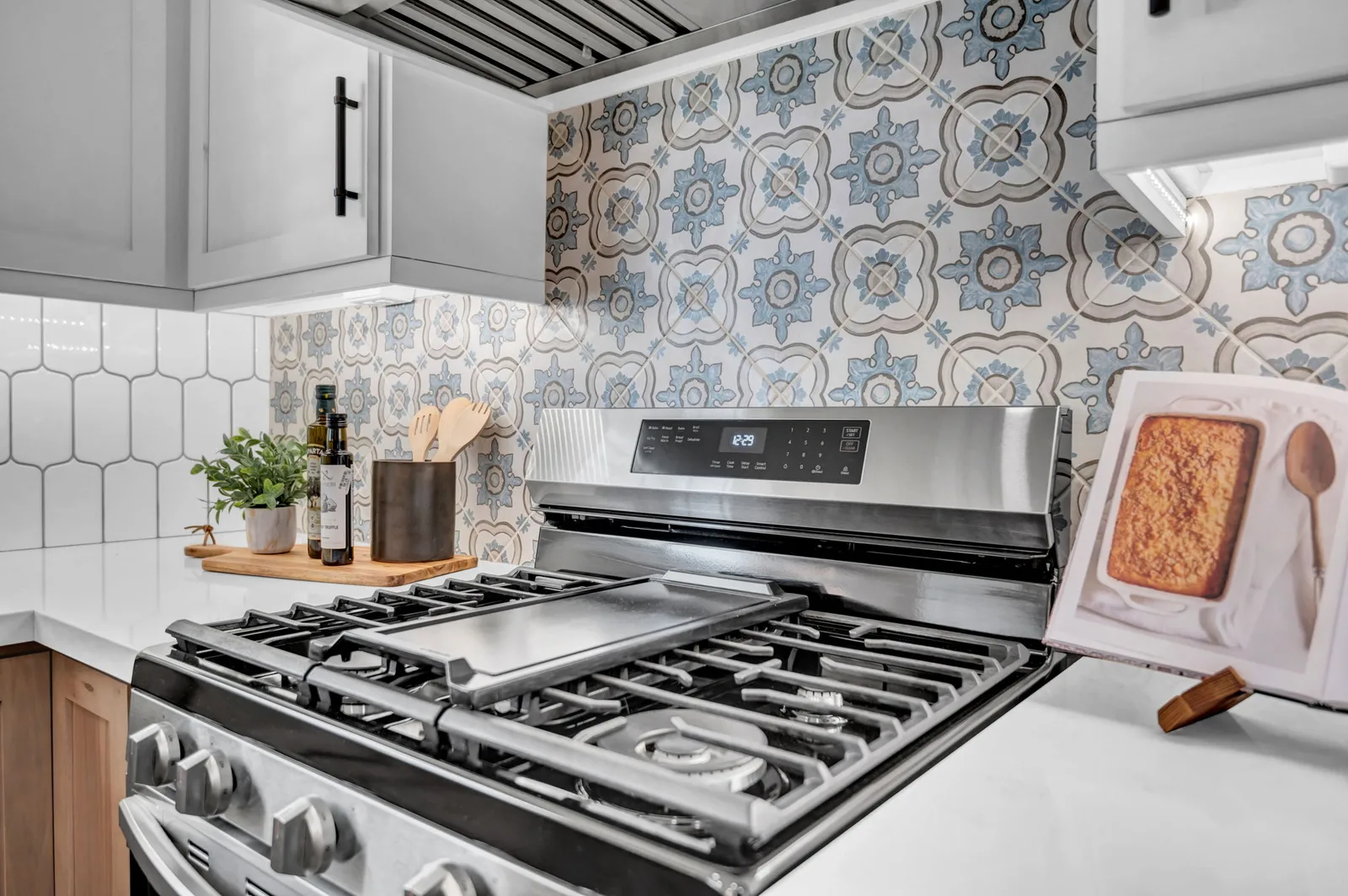 Gas range against a patterned tile backsplash in a remodeled kitchen.
