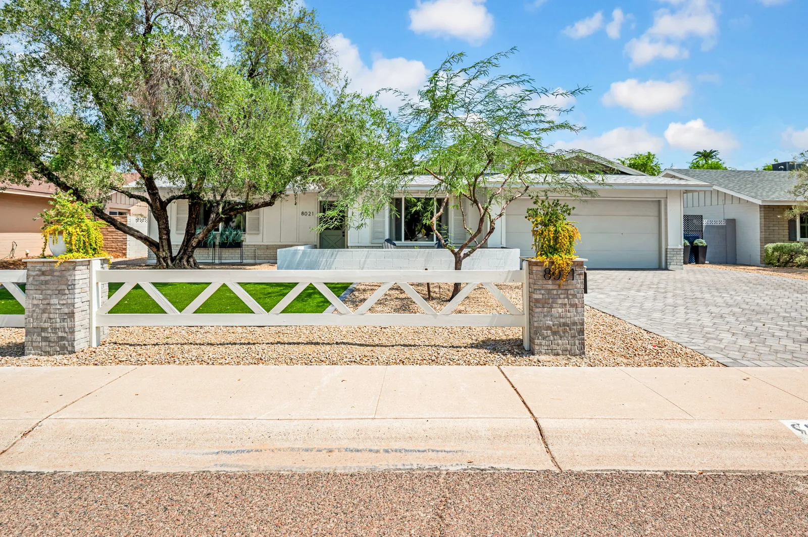 Ranch home behind a low painted block wall with a mature tree in the front yard.