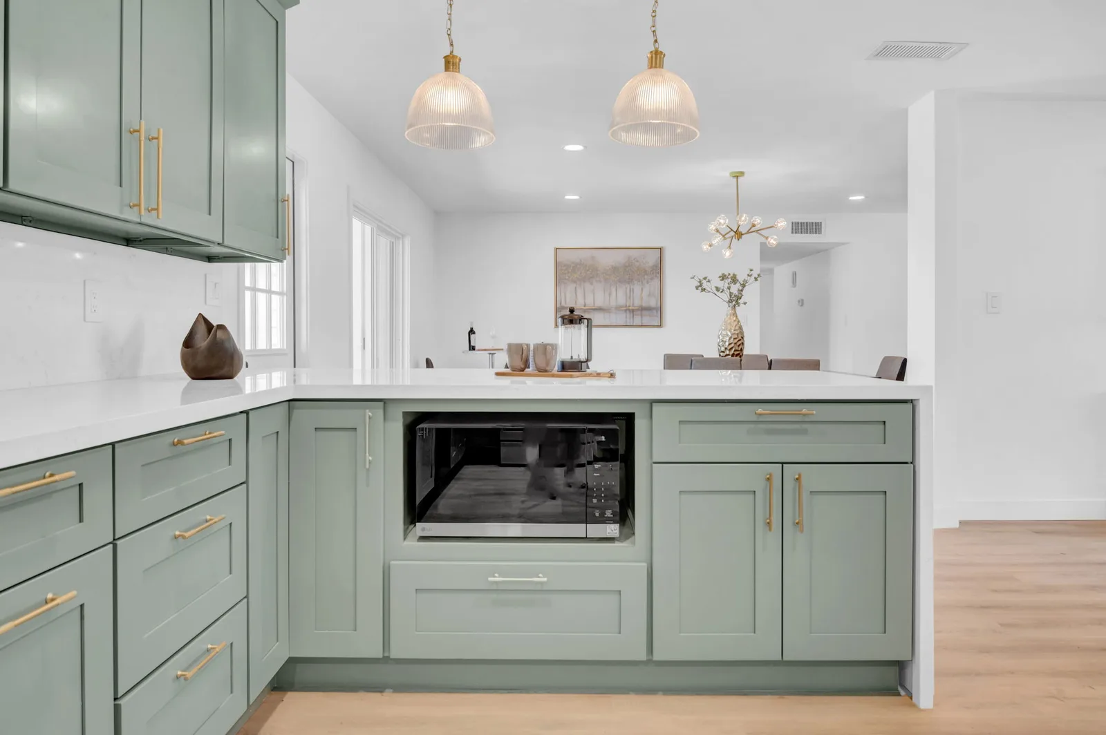 Sage L-shaped kitchen with built-in microwave and brass hardware.
