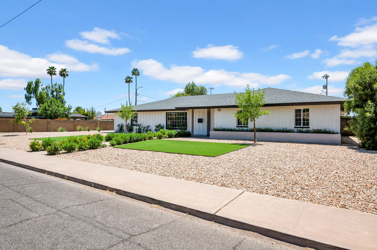 Long low ranch roofline seen from the street, palms and gravel yard in the afternoon sun.
