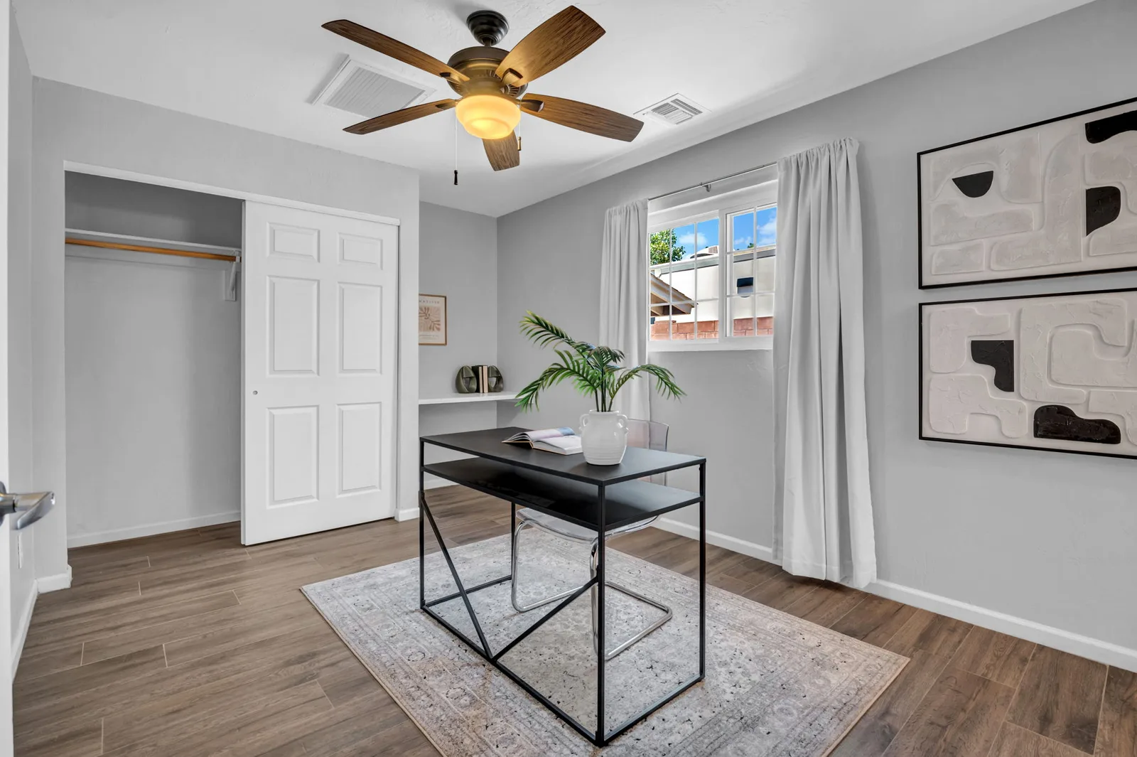 Home office nook with a slim desk, shutters and a closet behind.