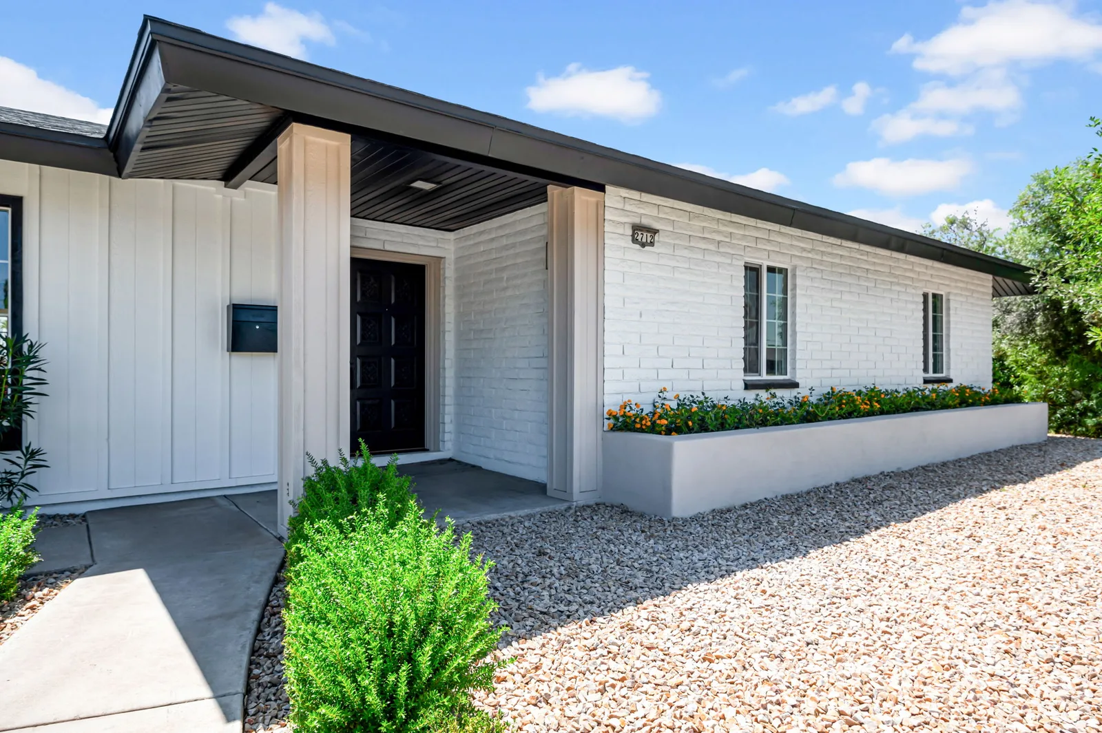 White painted brick ranch with a covered carport entry and clean modern landscaping.