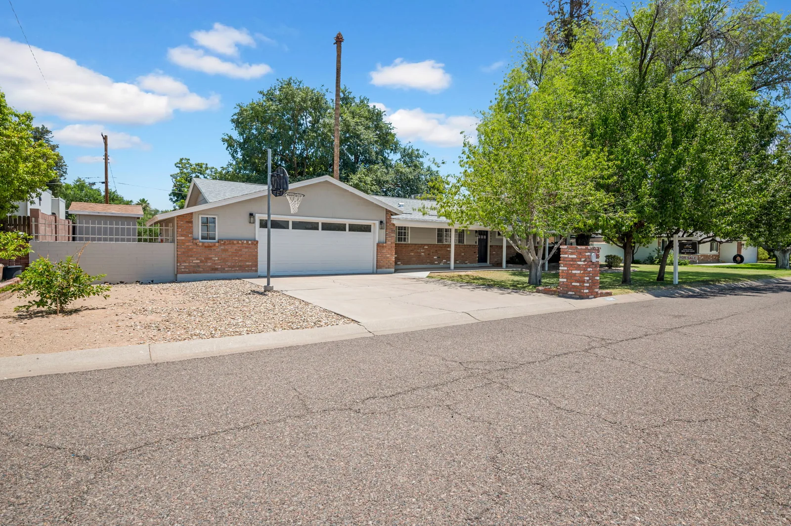 Brick ranch with a two-car garage and mature trees over a wide green front yard.