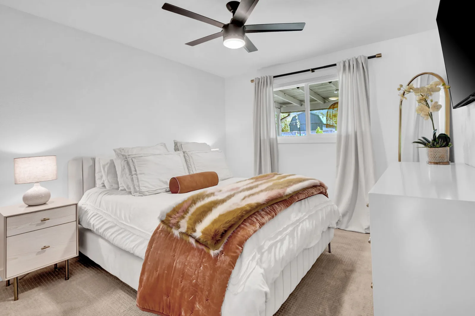 Primary bedroom with a rust throw and wide windows to the yard.